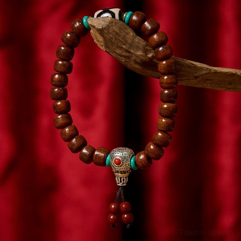 Tibetan three-eye Dzi bone bead bracelet with turquoise accents and red tassel on red velvet background