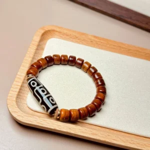 Tibetan bone Dzi bracelet on wooden tray showing warm reddish brown beads and patterned accent