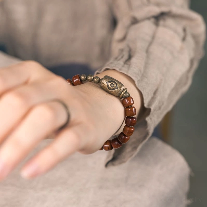 Tibetan bone Dzi bracelet worn on left wrist in casual hand pose against grey textile background, authentic daily wear styling