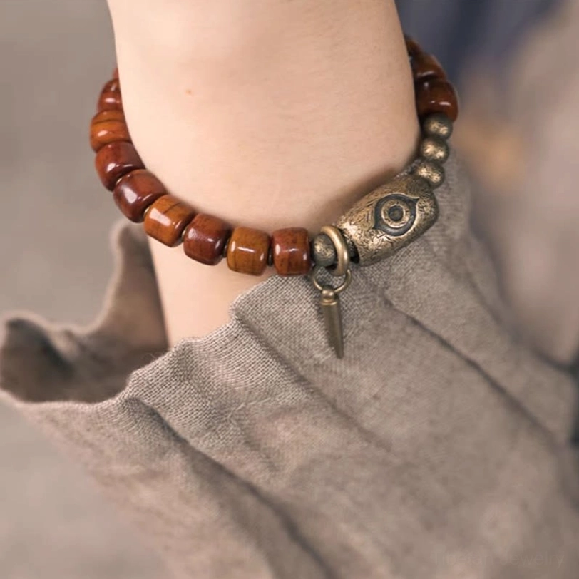 Close-up front view of Tibetan Dzi bone bracelet on right wrist with copper eye charm clearly visible against grey fabric