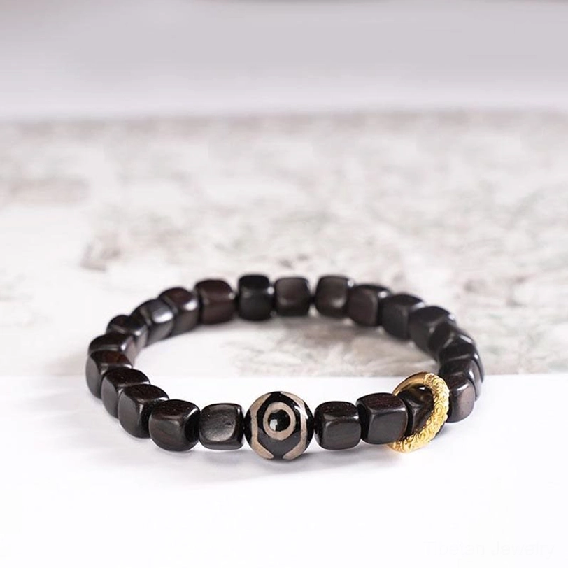 Tibetan ebony wood three-eye dzi bead bracelet angled flat lay shot with copper accent ring