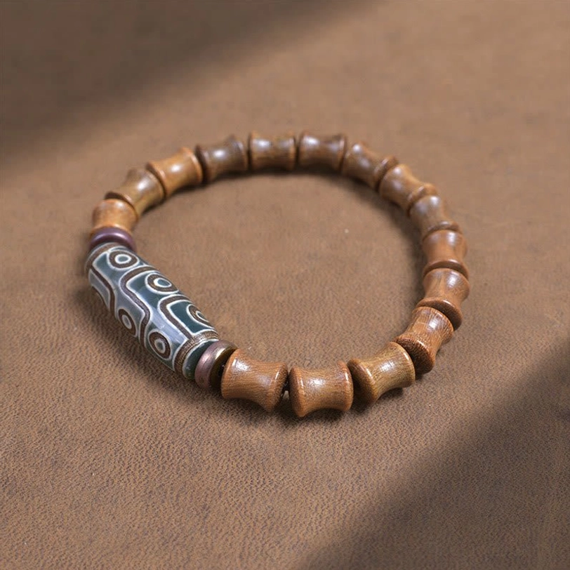 Tibetan nine-eye dzi green sandalwood bracelet laid flat on brown fabric showing round smooth beads with purple metal accents