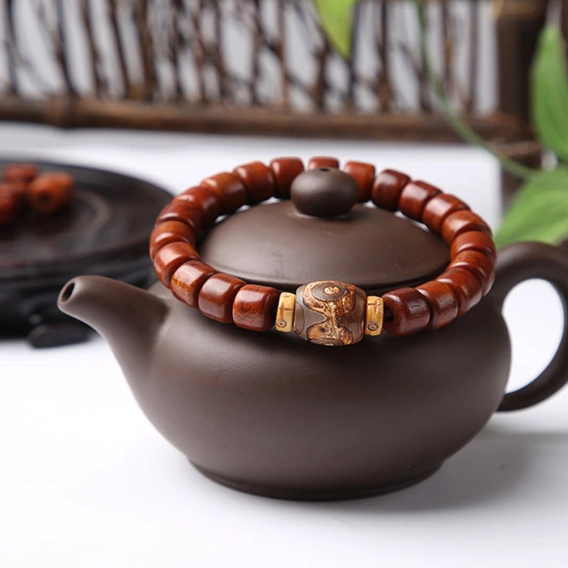 Tibetan bone bead bracelet with three-eyed dzi accent flat lay on traditional tea setting