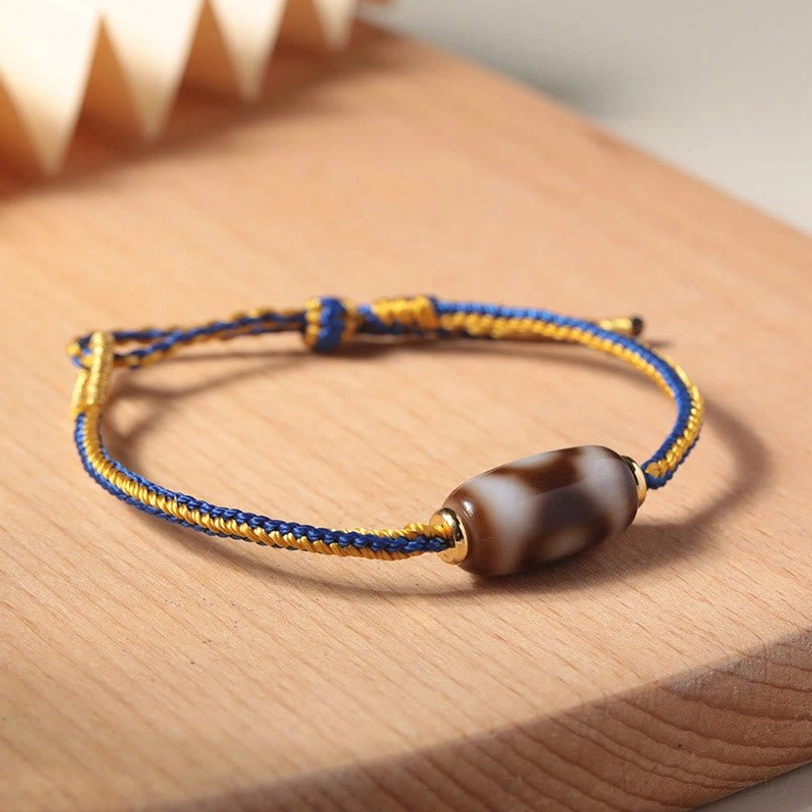 Tibetan Dzi bracelet three-quarter view on wooden tray, showing braided cord work and protective agate stone