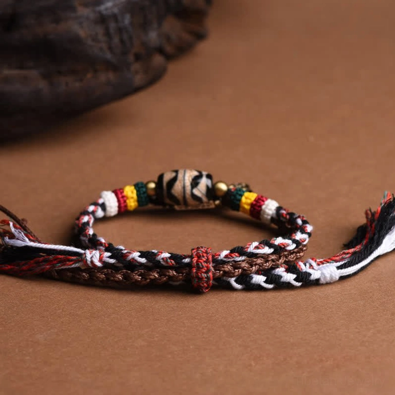 Side view of Tibetan braided Dzi bead bracelet featuring brown-toned woven rope, sacred Dzi bead, metal charm, and adjustable knot closure