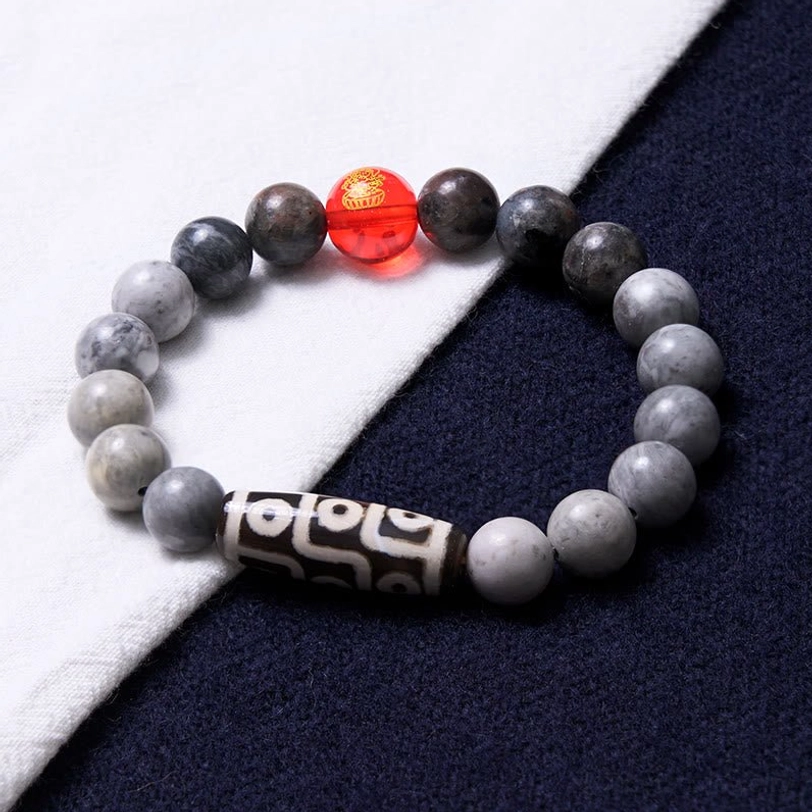 Nine-eye dzi picasso jasper healing bracelet on white cloth background, highlighting natural stone texture and vibrant red accent bead