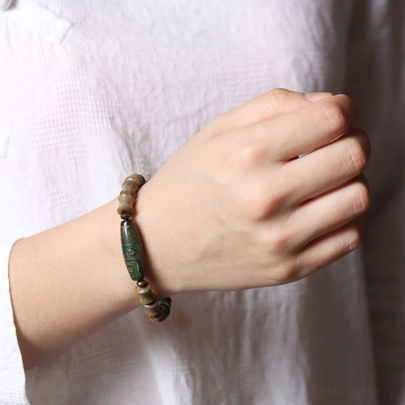 Nine-eye dzi green sandalwood bracelet worn on human hand close-up side view showing proper fit and wearing style