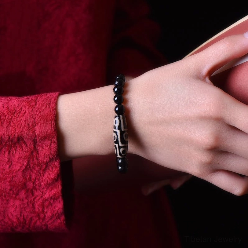 Close-up of nine-eye dzi bead bracelet worn on human wrist with red garment, showing proper fit and clear nine-eye pattern on natural agate stone