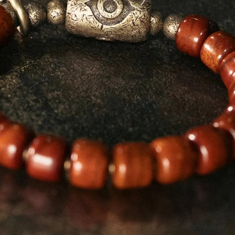 Top-down macro view of Tibetan bone bead bracelet highlighting large bronze eye Dzi charm and decorative metal spacer beads
