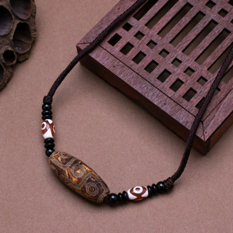 Brown vintage Tibetan dzi bead necklace with carved stone patterns and black wax cord on wooden board - grounding spiritual amulet