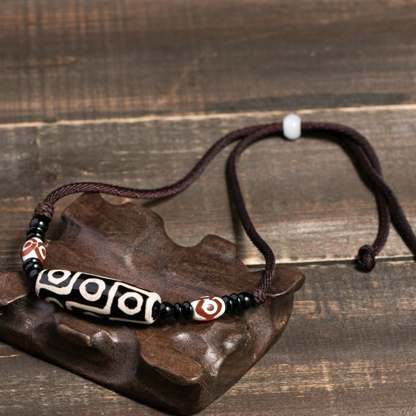 Tibetan nine-eye dzi bead necklace with brown adjustable cord on wooden display stand - prosperity and protection talisman