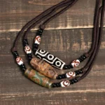 Collection of Tibetan nine-eye dzi bead necklaces in brown and black displayed on vintage wooden table - authentic protective amulet pendants