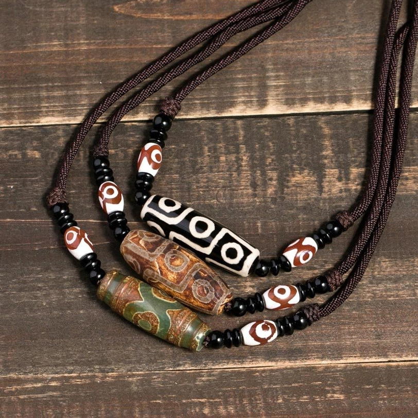 Collection of Tibetan nine-eye dzi bead necklaces in brown and black displayed on vintage wooden table - authentic protective amulet pendants