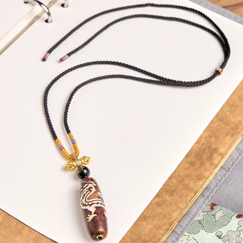 Overhead flat lay view of Tibetan nine-eye dzi necklace showing complete pendant and braided cord design
