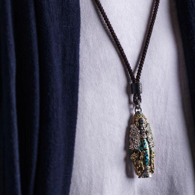 Complete Tibetan necklace with dzi pendant displayed on white shirt and navy fabric, showing full black braided cord and ornate pendant design