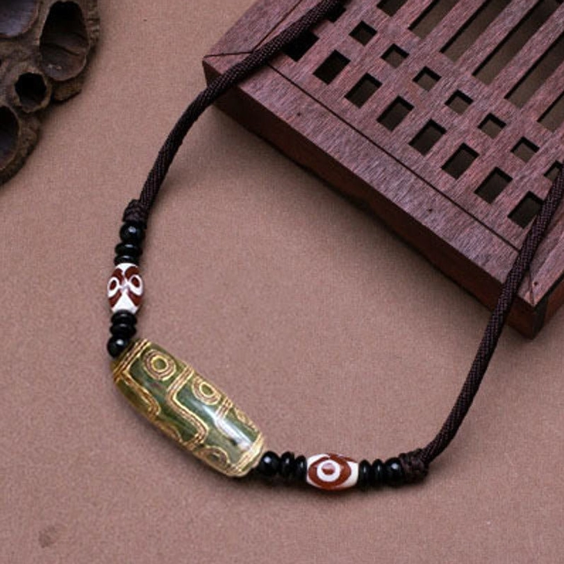 Green vintage Tibetan dzi bead necklace with black wax cord and red-white spacers on carved wooden board - natural stone amulet