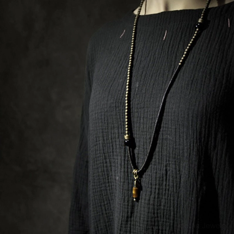 Long Tibetan Dzi bead necklace with layered black beads and tiger eye drop pendant, worn on mannequin torso