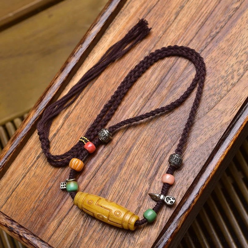 Nine-Eye Dzi bead copper necklace with bone pendant and colorful spacer beads on wooden display tray
