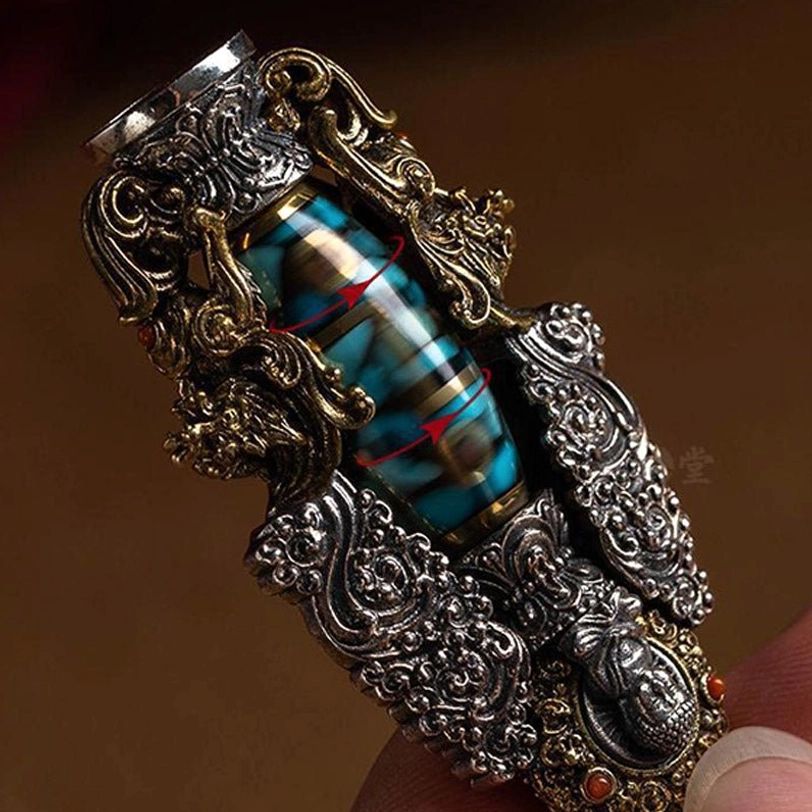 Close-up of Tibetan dzi bead pendant held by fingers, showing dragon-themed metal carvings, dual metal tones, and rotatable bead core