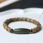 Tibetan nine-eye dzi green sandalwood bracelet overhead view on ceramic tray showing bamboo-cut wooden beads and green patterned dzi bead