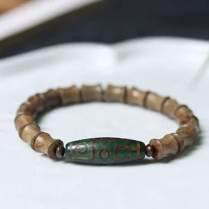 Tibetan nine-eye dzi green sandalwood bracelet overhead view on ceramic tray showing bamboo-cut wooden beads and green patterned dzi bead