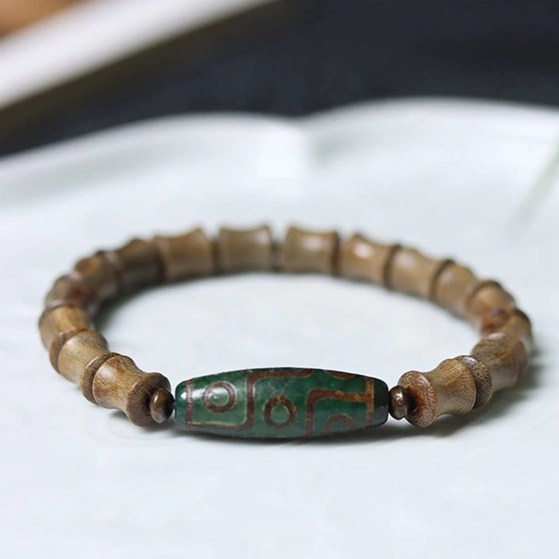 Tibetan nine-eye dzi green sandalwood bracelet overhead view on ceramic tray showing bamboo-cut wooden beads and green patterned dzi bead