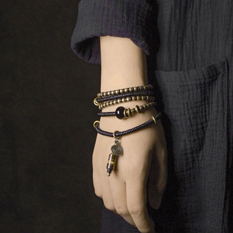 Triple-layer Tibetan Dzi bead bracelets on hand with hanging protective pendant, close-up detail shot