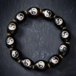 Tibetan Dzi Bead Yin Yang bracelet flat lay showing black agate beads with white Yin Yang symbols and gold metal spacers on dark grey surface
