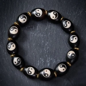 Tibetan Dzi Bead Yin Yang bracelet flat lay showing black agate beads with white Yin Yang symbols and gold metal spacers on dark grey surface