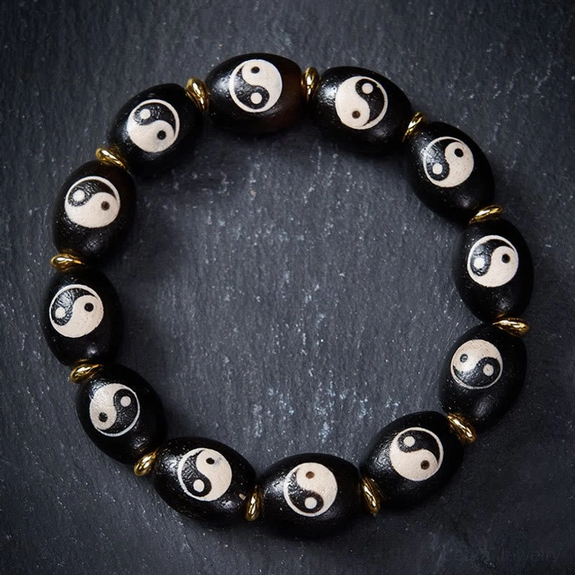 Tibetan Dzi Bead Yin Yang bracelet flat lay showing black agate beads with white Yin Yang symbols and gold metal spacers on dark grey surface