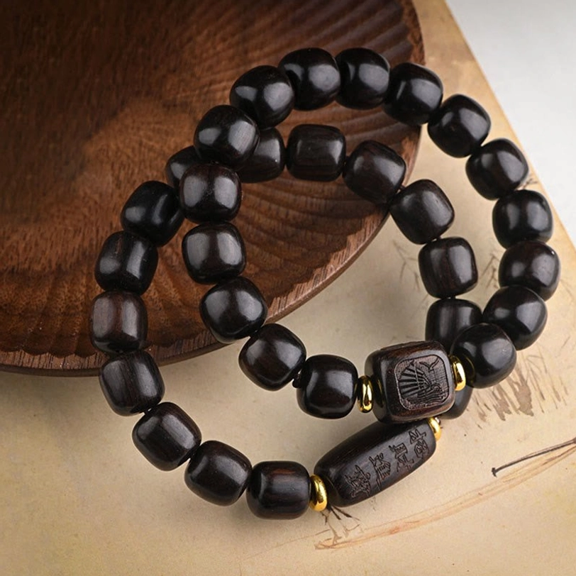 Tibetan ebony wood barrel bead bracelet flat lay on wooden coaster with carved square decorative accents and gold brass spacers