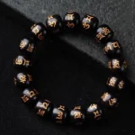Tibetan Om Mani Padme Hum ebony wood bracelet with hand-engraved golden Sanskrit mantras on 12mm barrel beads, displayed on dark stone background