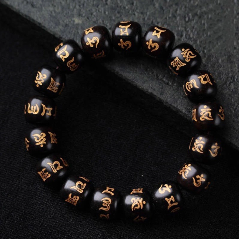 Tibetan Om Mani Padme Hum ebony wood bracelet with hand-engraved golden Sanskrit mantras on 12mm barrel beads, displayed on dark stone background