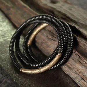 Multi-strand ebony wood beaded bracelet with curved brass metal accents, oblique top-down view on wooden surface