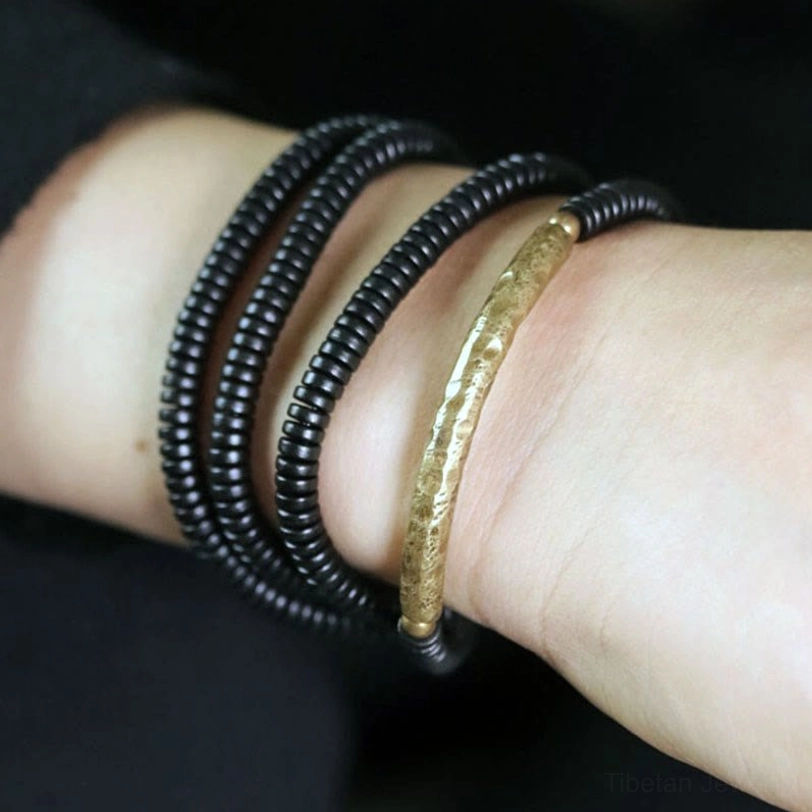 Finished ebony wood bracelet with brass curved accent worn on wrist, side view showing protective multilayer wrapping