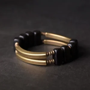 Tibetan ebony wood and brass double layer bracelet displayed on dark concrete background, showing dual-row design with matte gold metal bars and dark square beads from top-down angle