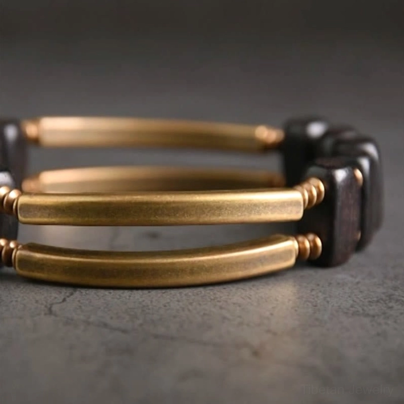 Double layer tibetan ebony and brass bracelet low angle top-down view on dark grey concrete, showing three parallel gold brass bars with dark ebony bead sets in stacked dual-row design