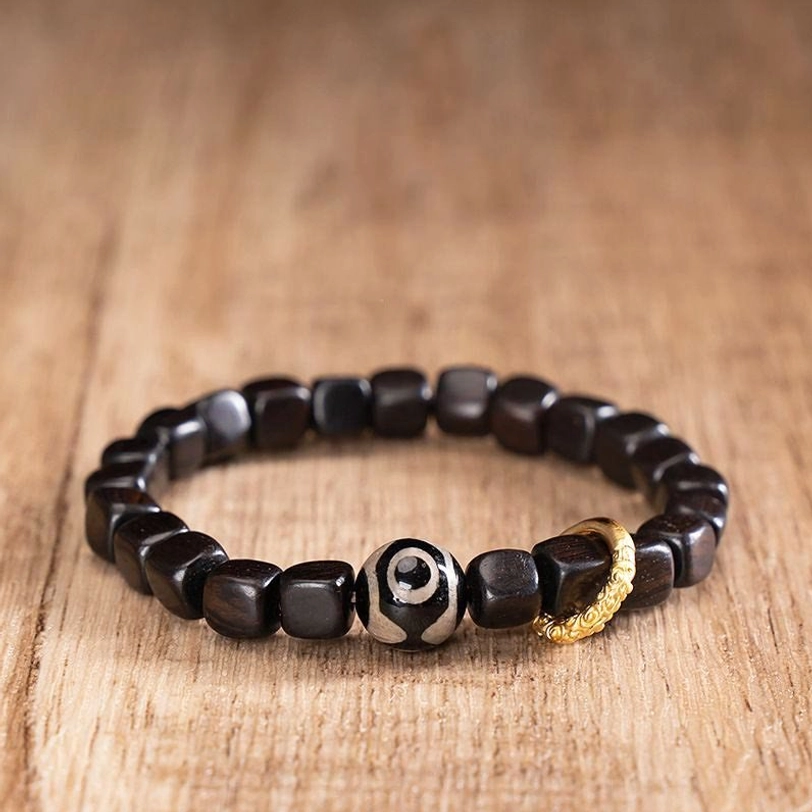 Tibetan ebony wood and three-eye dzi bead bracelet with gold metal ring on natural wooden surface