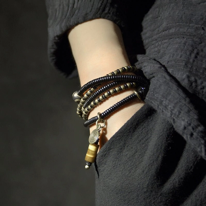 Multi-layer Tibetan ebony wood Dzi bracelet stack worn on wrist, close-up side view on dark linen background