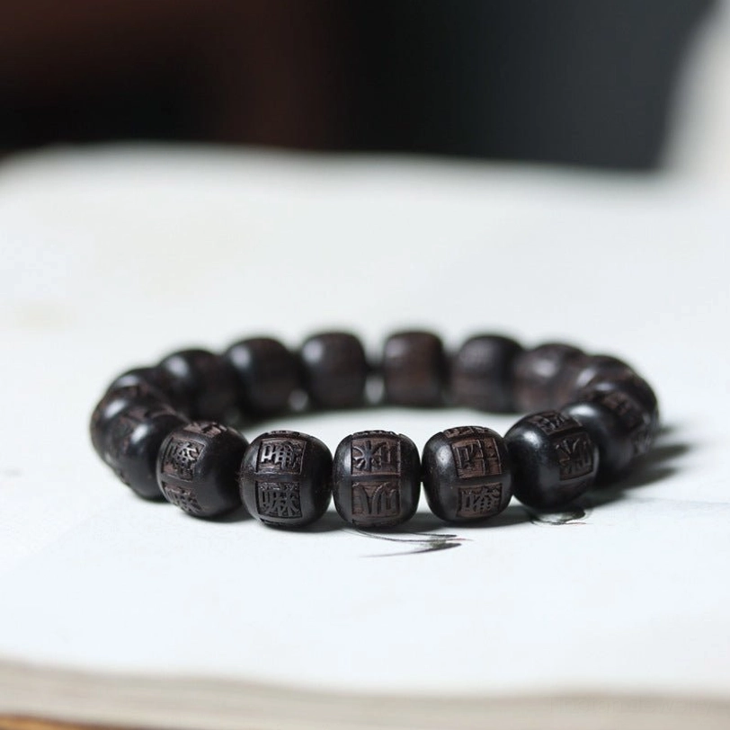 Tibetan ebony wood Om Mani Padme Hum engraved prayer bracelet with mantra beads on book flat lay