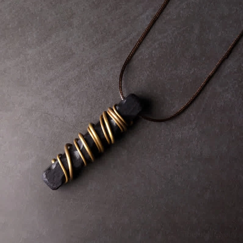 Ebony wood Tibetan necklace pendant shot at oblique angle, highlighting the brass wire coils and brown wax cord construction