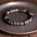Tibetan ebony wood copper bracelet overhead display showing full circular bead arrangement with dark wood beads and vintage bronze carved spacers on metal tray