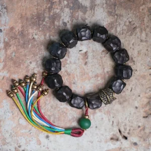 Tibetan ebony wood copper mala bracelet flat lay with peace tassel on stone surface
