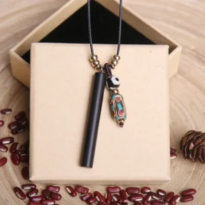 Tibetan ebony wood dzi bead necklace with black wax cord in gift presentation on wooden surface with decorative elements