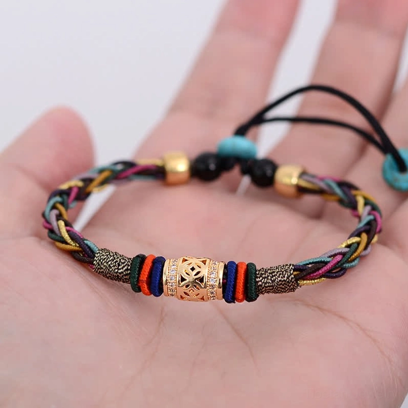 Red string Tibetan bracelet held in human palm showing adjustable knot, carved center bead, and multicolor braided cord for wrist wear