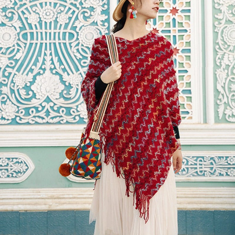 Ethnic tibetan knit poncho shawl with asymmetric tassel hem and zigzag woven pattern in front of retro carved window