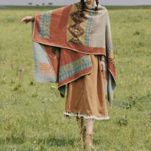 Oversized tribal poncho cloak full body side view showing geometric ethnic print and warm woven fabric in natural pasture setting