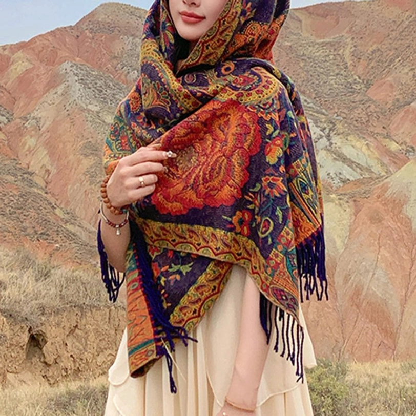 Head wrap ethnic shawl worn as hooded covering in outdoor mountain setting, intricate floral motifs detail visible