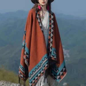Full-body front view of ethnic geometric wrap shawl with white inner dress, showing decorative collar trim and tassel hem against mountain backdrop