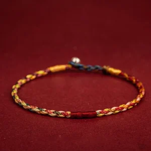 Five-color Tibetan protection bracelet flat lay showing multicolored braided threads with metal clasp on wine red background